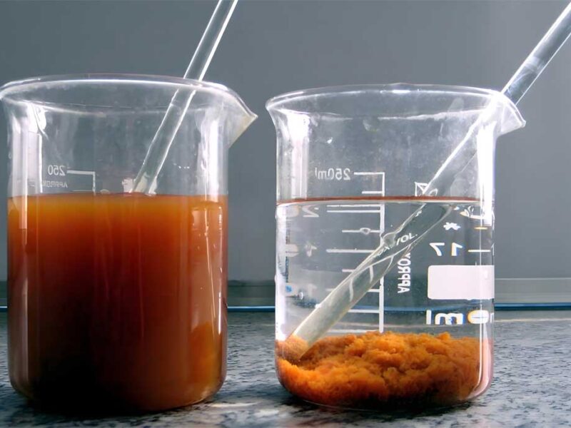 Flocculant powder being added to a beaker of water, causing suspended particles to clump together and settle at the bottom.
